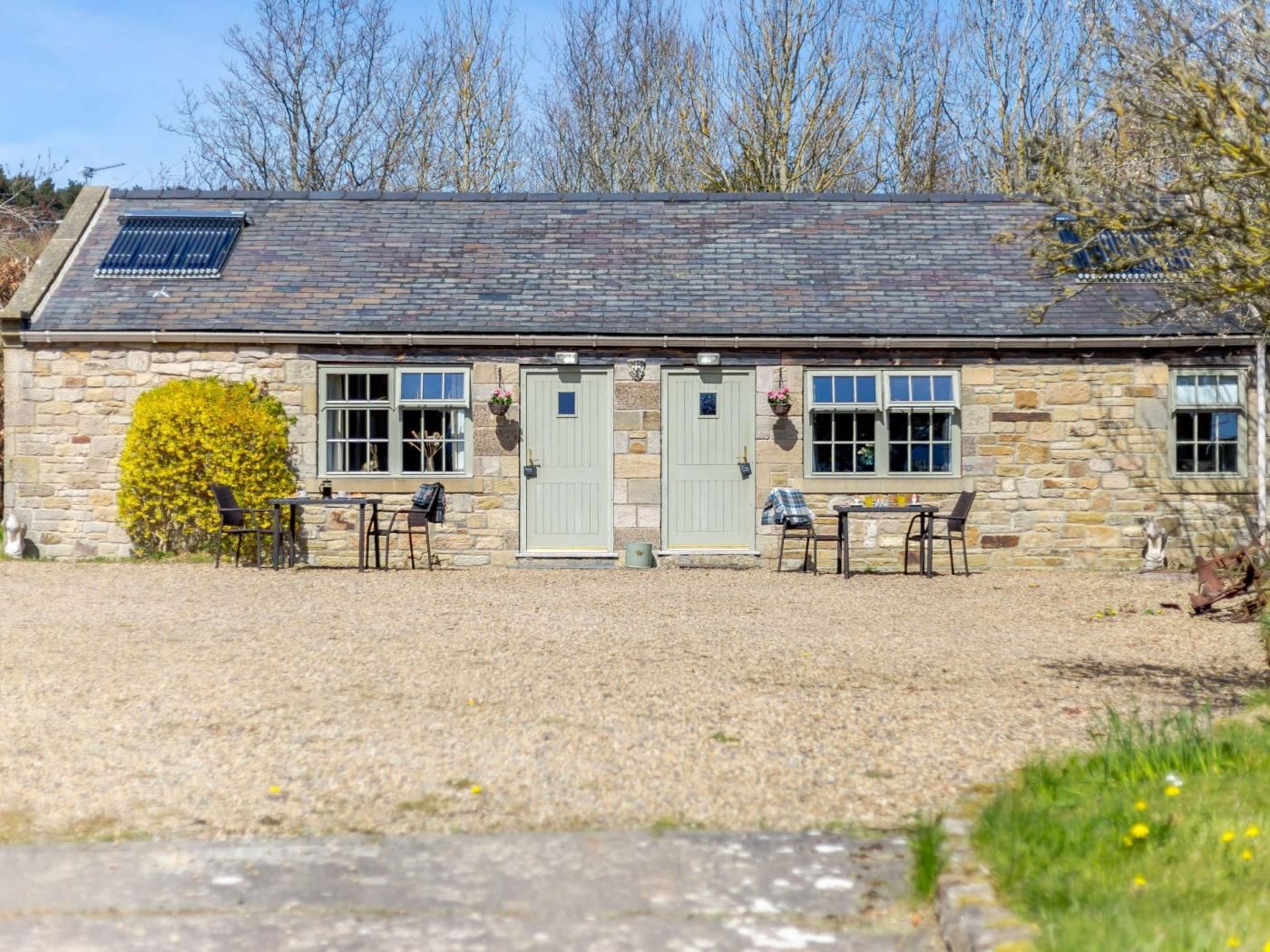 Un bâtiment en pierre avec deux portes, des fenêtres et une petite table entourée de chaises à l’extérieur.
