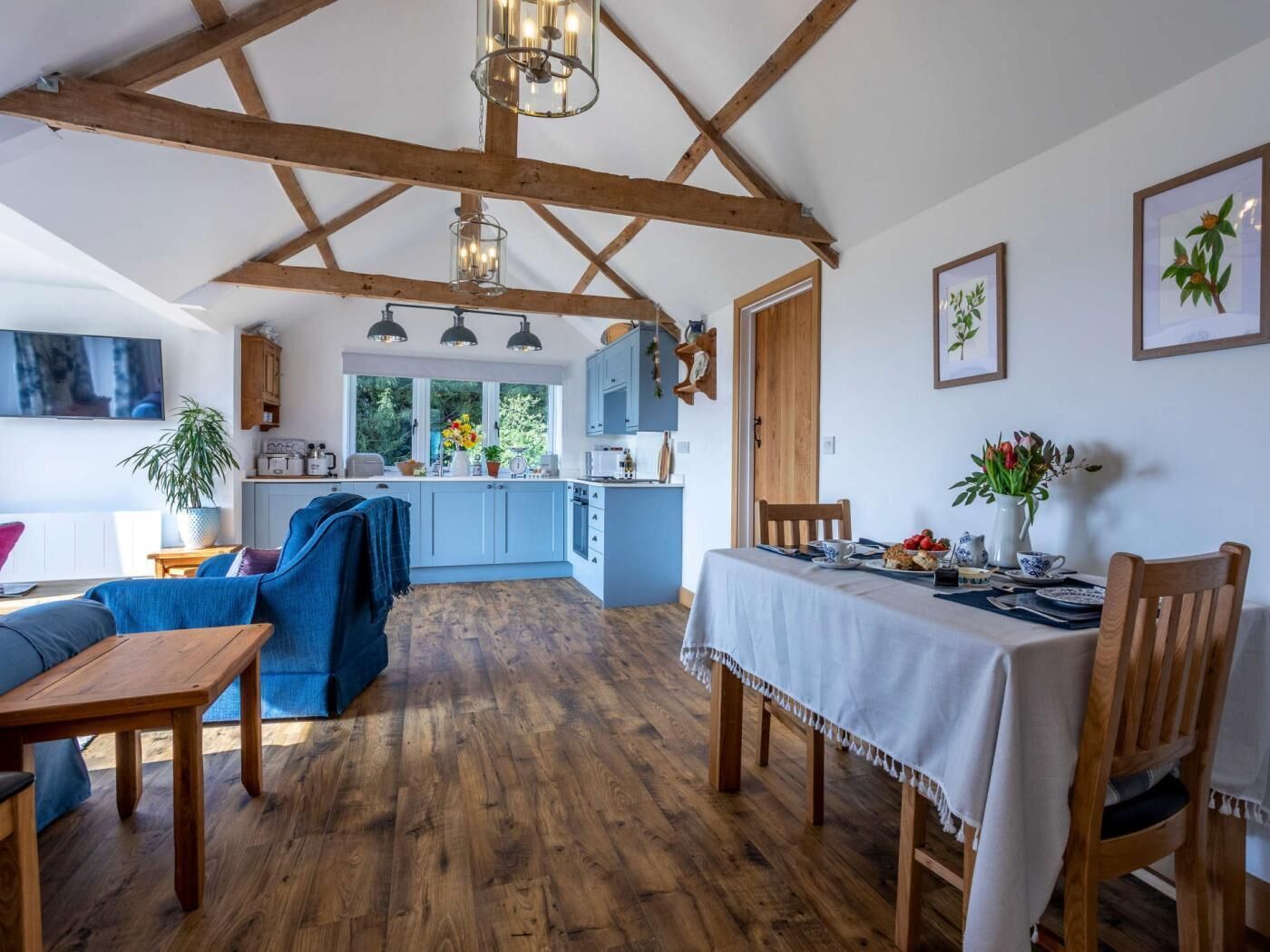A spacious living area with a wooden ceiling, a dining table set for two, and a kitchen in the background.