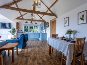 A spacious living area with a wooden ceiling, a dining table set for two, and a kitchen in the background. - 1 Bed in Axminster (oc-82604) (Tytherleigh)