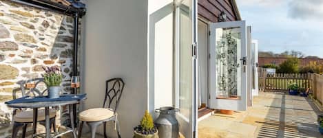 A patio with a table and chairs, a potted plant, and a sliding glass door leading to a garden.