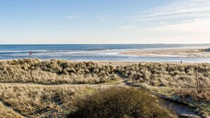 Een kustlandschap met een strand, begroeide duinen en een heldere lucht.