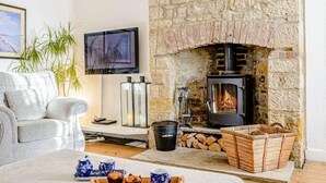 Een gezellige woonkamer met een stenen openhaard, een comfortabele bank, een televisie en een dienblad met muffins.