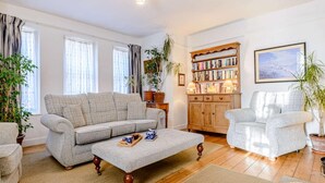 Een woonkamer met een bank, fauteuil, houten kast en een boekenkast.