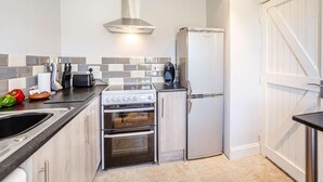 A compact kitchen with a built-in oven, a refrigerator, and a gas stove. - 2 Bed in Berwick-upon-tweed (oc-81273) (Berwick-upon-Tweed)