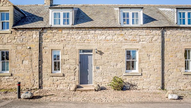 A stone building with a central entrance, multiple windows, and a chimney. - 2 Bed in Berwick-upon-tweed (oc-81273) (Berwick-upon-Tweed)