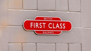 En brittisk skylt med texten "First Class Railways" monterad på en vit tegelvägg.