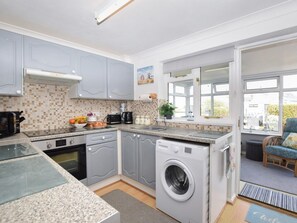 A compact kitchen with grey cabinets, a built-in oven, a washing machine, and a window with a view. - 2 Bed in Norwich (oc-81322) (Walcott)