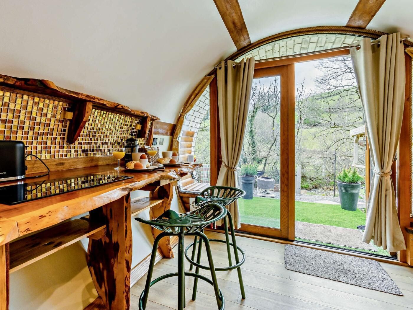 A cozy kitchen with a wooden table, bar stools, and a view of the garden.
