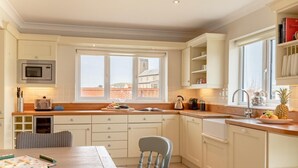 A kitchen with a dining table, chairs, a microwave, a toaster, a kettle, and a window with a view of buildings. - 4 Bed in Cromer (oc-81469) (West Runton)