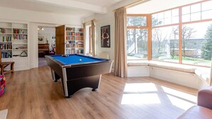 Een pooltafel in een ruimte met grote ramen, boekenkasten en een piano.