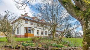 Een groot, wit huis met een tuin met een stenen muur ertegen.