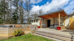 Een overdekt terras met buitenmeubilair, een houten terras en een gebouw met schuine kap.