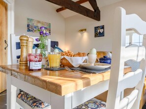 A breakfast setting with a wooden table, a vase of flowers, a basket of croissants, a glass of orange juice, and a jar of jam. - 1 Bed in Challacombe (oc-81477) (Challacombe)