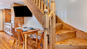 Eine Holztreppe führt zu einem Essbereich mit einem Tisch, der für eine Mahlzeit gedeckt ist, einem an der Wand befestigten Fernseher und Holzschränken im Hintergrund.