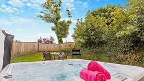 Ein Whirlpool mit einer Holzdielen-Terrasse, einem Tisch mit Stühlen und einem Holzzaun im Hintergrund.