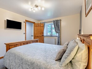 Quarto com cama, televisão, guarda-roupa de madeira, janela com cortinas e luminária no teto.
