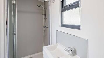 A bathroom with a shower, a sink, and a window.