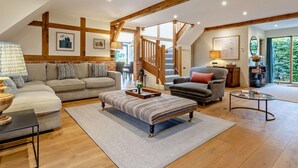A spacious living room with a high ceiling, exposed wooden beams, a staircase, and a large window providing a view of greenery. - 2 Bed in Hereford (oc-82095) (Lulham)