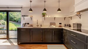 A modern kitchen with dark cabinets, a large island, pendant lighting, and a view of the outdoors. - 2 Bed in Hereford (oc-82095) (Lulham)
