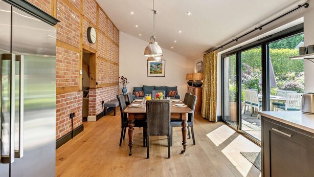 A modern kitchen with a brick wall, wooden flooring, a dining area with a table and chairs, and a large window offering a view of the outdoors. - 2 Bed in Hereford (oc-82095) (Lulham)