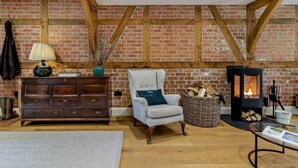 A cozy room with exposed brick walls, a wooden ceiling, a fireplace, a striped armchair, a wooden dresser, and a lamp. - 2 Bed in Hereford (oc-82095) (Lulham)