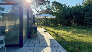 A wooden deck with a glass enclosure, potted plants, and a patio umbrella. - New timber house with cozy terrace near the beach (Hals)
