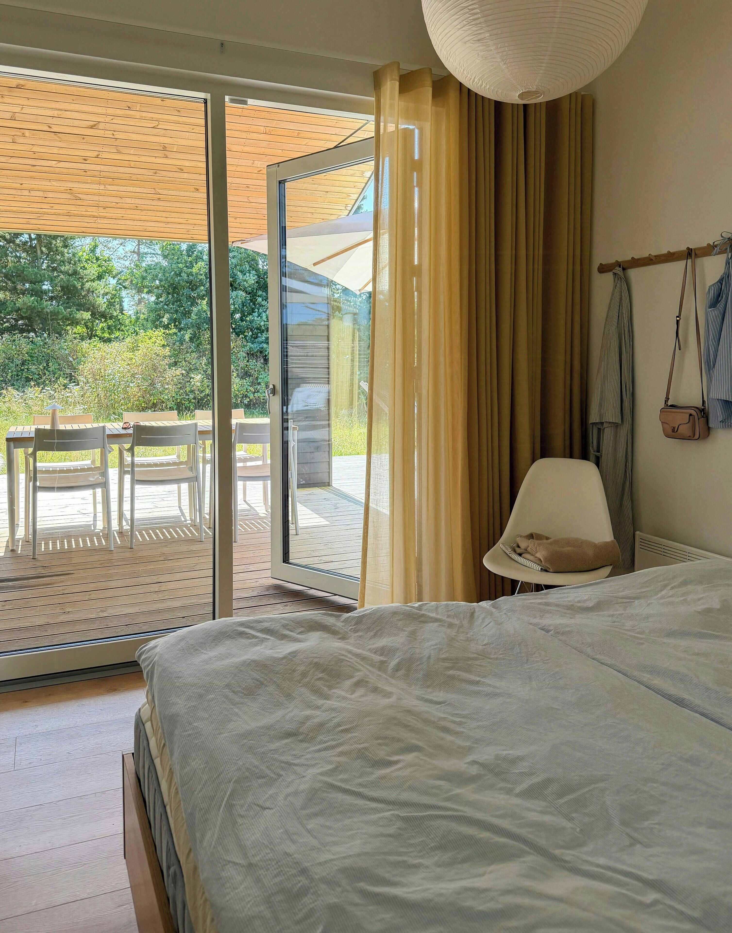 Une chambre à coucher comprenant un lit, une chaise, une table et donnant sur l’extérieur grâce à une porte-fenêtre coulissante.