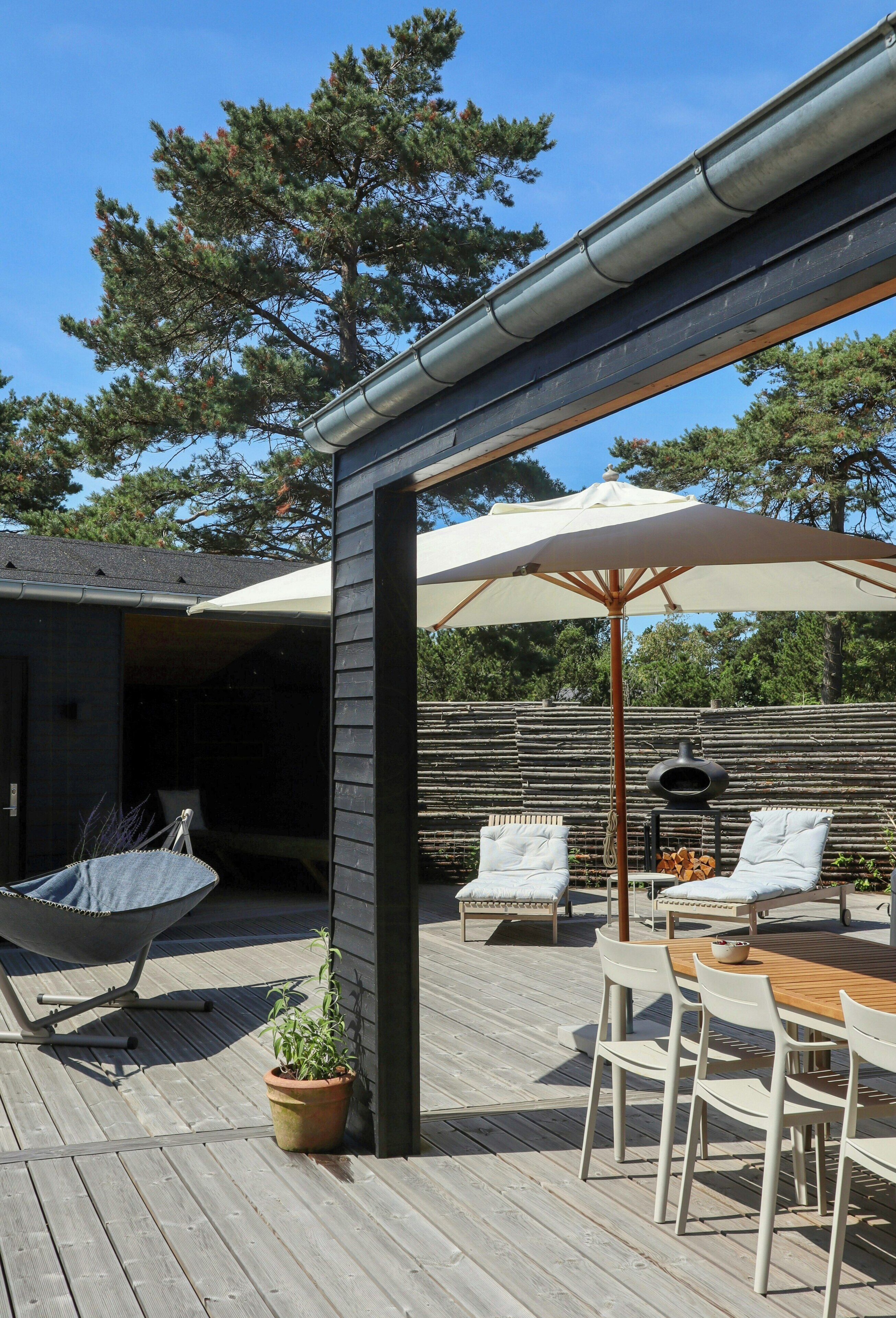 An outdoor patio with a wooden deck, a hammock, a table with chairs, and a barbecue grill.
