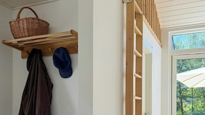 Une pièce avec un banc en bois, une étagère fixée au mur avec un panier et des chapeaux, et une échelle en bois menant à une porte.