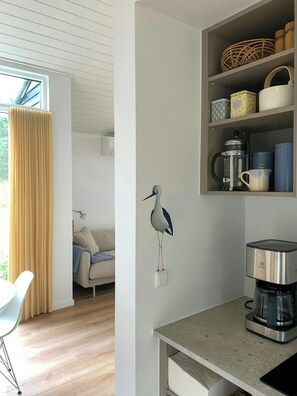 A modern kitchen with a coffee maker, shelves with containers, and a wall-mounted bird decoration. - New timber house with cozy terrace near the beach (Hals)