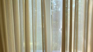 Une chambre avec un lit, un plancher en bois et des rideaux légers qui laissent passer la lumière naturelle.