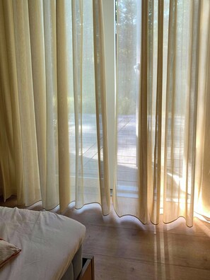 A room with a bed, wooden flooring, and sheer curtains allowing natural light. - New timber house with cozy terrace near the beach (Hals)