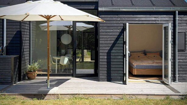 Une maison moderne dotée d’une terrasse, d’une porte-fenêtre coulissante donnant sur une chambre et d’un parasol pour la terrasse.