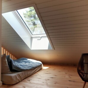 A room with a sloped ceiling, a skylight, a bed with pillows, and a chair. - New timber house with cozy terrace near the beach (Hals)