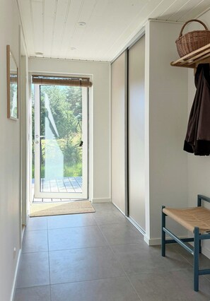 Een hal met een schuifdeur naar een balkon, een bankje en een mand aan de muur.