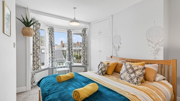 Ett sovrum med en säng, ett fönster med gardiner, en växt och en drömfångare på väggen.