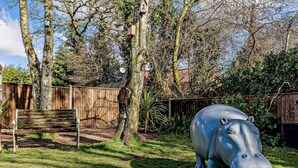 Ein Garten mit einer Holzbank, einer großen, blauen Hipposkulptur und einem Holzzaun.