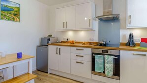 Une cuisine moderne avec des armoires blanches, un plan de travail en bois, un four encastré et un petit réfrigérateur.