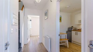 Un couloir menant à une cuisine avec des meubles blancs, un banc en bois et un radiateur.