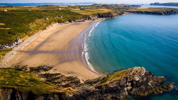 Un paysage côtier avec une plage de sable, des affleurements rocheux et une vue dégagée sur la mer.