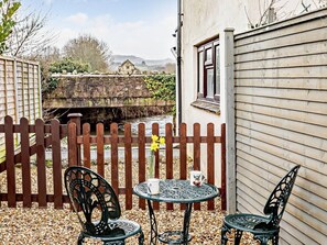 Eine Terrasse mit zwei Stühlen und einem Tisch, ein Holzzaun und eine Steinmauer.