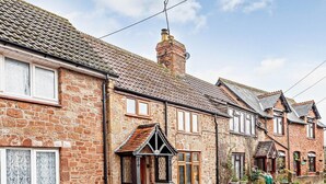 A row of stone houses with pitched roofs, a visible chimney, and a small front garden with potted plants. - 1 Bed in Watchet (oc-81240) (Washford)