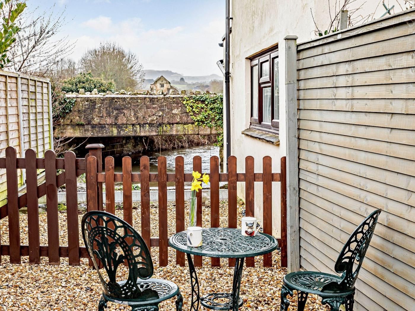 A patio with two chairs and a table, a wooden fence, and a stone wall.