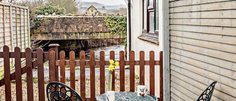 Un patio con dos sillas y una mesa, cerca de una valla de madera y un muro de piedra.