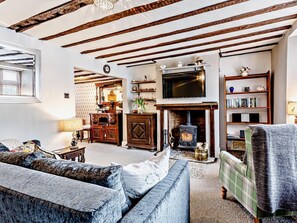Ein Wohnzimmer mit freiliegenden Holzbalken, Kamin, Fernseher und Bücherregal.