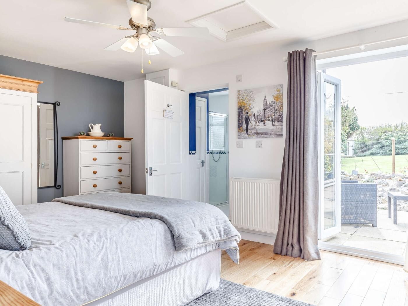 A bedroom with a bed, a dresser, a ceiling fan, a door, and a view of the outdoors.
