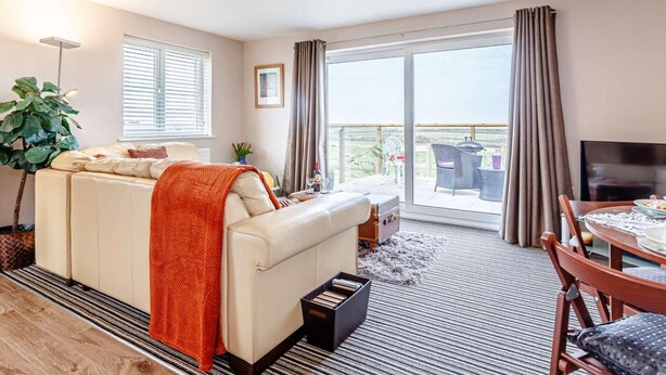 A modern living room with a sofa, a dining table, a TV, and a balcony with a view. - 1 Bed in Bude (oc-82365) (Jacobstow)