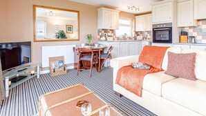A living room with a sofa, a TV, and a dining area with a table and chairs. - 1 Bed in Bude (oc-82365) (Jacobstow)