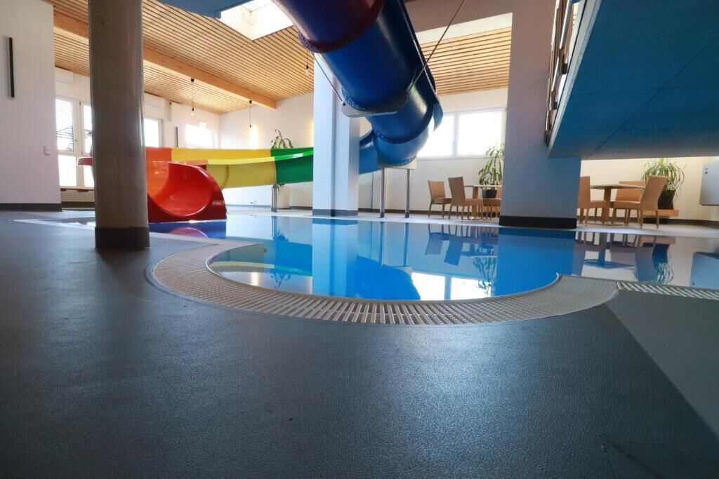 An indoor swimming pool with a slide, seating area, and wooden ceiling.
