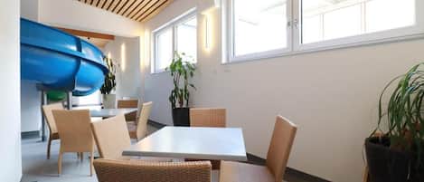 Un comedor con una mesa y sillas, un tobogán azul y plantas en macetas.